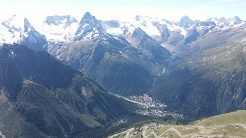 Aerial drone fly-forward shot of majestic snowy mountain peaks and a green resor Stock Footage 336957862