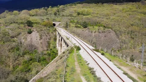 Aerial drone flying backward over empty railway tracks crossing a green moun Stock Footage 337702596