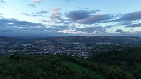 Aerial Drone Flying Backwards Over Forest and Town at Sunset, Wales Stock Footage 343578250