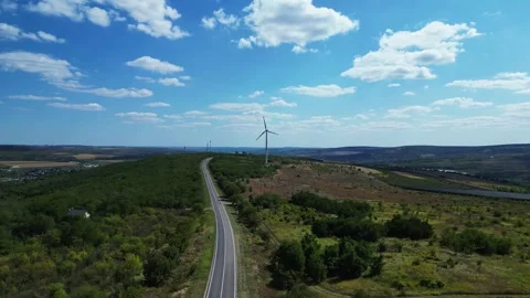 Aerial drone flying toward wind turbines over green hills and road Stock Footage 319919692
