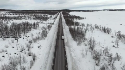 Aerial drone footage capturing a car journey along a snowy, secluded Nordic road Stock Footage 330376530