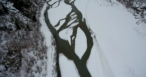 Aerial drone footage looking down on icy river flowing through snowy valley 库存影片 117907152