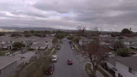 Aerial: Drone Forward Beautiful View Of Roofed Houses In City By Mountains Under Stock Footage 264203477