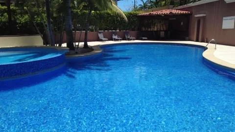 Aerial drone forward tracking shot over resort swimming pool with lounge chairs. Stock Footage 333657824