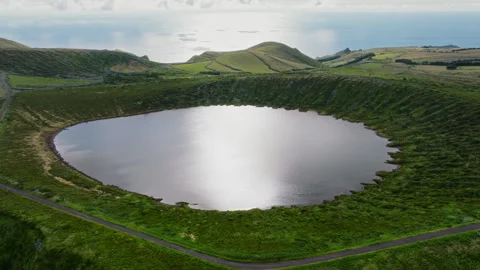 Aerial drone high-angle shot of a volcanic crater lake reflecting the sun, with Vidéo 335245482