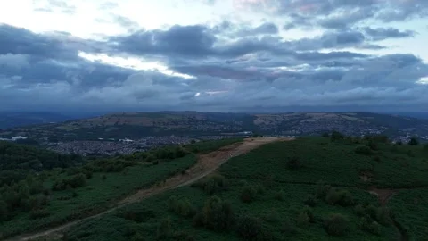 Aerial Drone Over Green Forest and Distant Town Beneath Grey Clouds, Wales Stock Footage 343578252