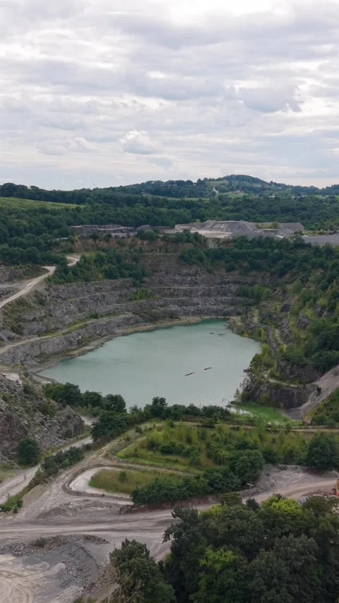 An aerial drone perspective showing an active rock quarry with a deep water 動画素材 345154932