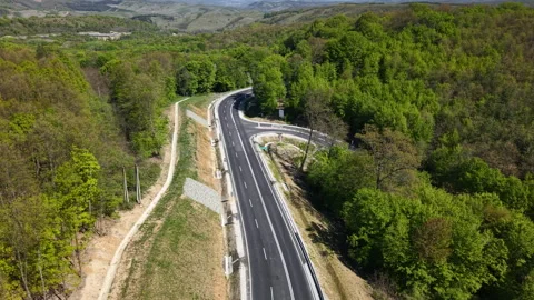 An aerial drone perspective shows a winding asphalt highway cutting through a Stock Footage 334138636