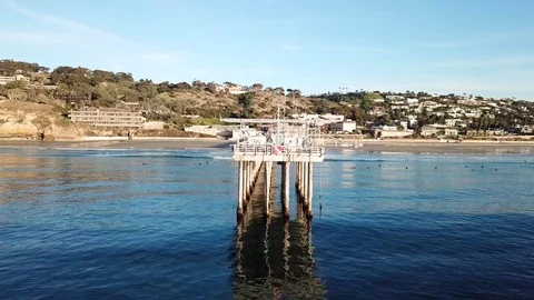 Aerial drone positioned off end of pier slowly rises while surfers surf on sides Stock Footage 85453360