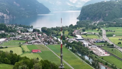 Aerial drone pulls back from cell tower over Swiss alps lake village 스톡 동영상 345620502