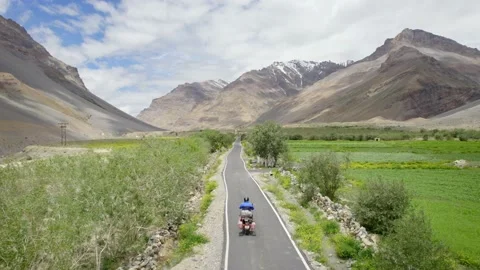 Aerial drone shot of biker on empty road passing by green farms in valley. Video stock 200813676