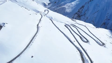 Aerial drone shot displaying a mesmerizing view of a snow-lined curvy road in Stock Footage 304952336