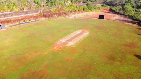 Aerial drone shot of an empty cricket pitch and field surrounded by lush Видео 331041678