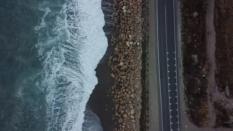 Aerial drone shot flying over a seaside road as waves crash against the rocks Stock Footage