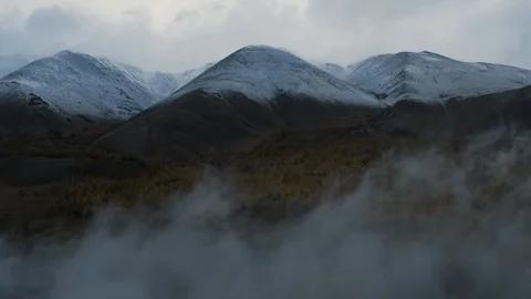 Aerial drone shot of forest valley and snowy mountain range through low cloud Stock Footage 100040428