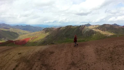 Aerial drone shot of a girl in an authentic rainbow poncho hiking on a mountain Stock Footage 105887053