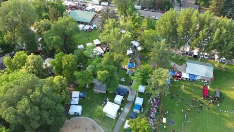 Aerial drone shot looking down at tents set up in small town park for festival Stock Footage 231511406
