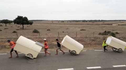 Aerial drone shot of people pulling camping carts on asphalt road amidst ag.. Stock Footage 260389845