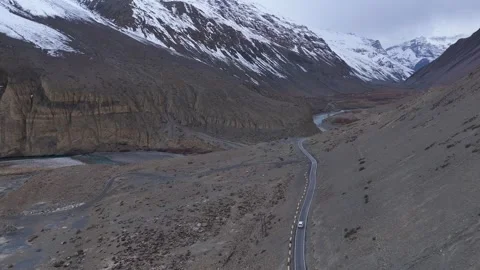 Aerial drone shot showcasing the changing landscape of Spiti as a white car Stock Footage 304950449