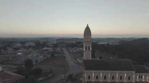 Aerial drone side view of illuminated church dividing city and nature at dawn Vídeos de archivo 334126696