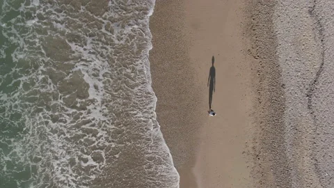 AERIAL DRONE TOP DOWN MAN WALKING ALONE IN BEACH WITH BIG SHADOW AND STRONG TIDE Stock Footage 130339256