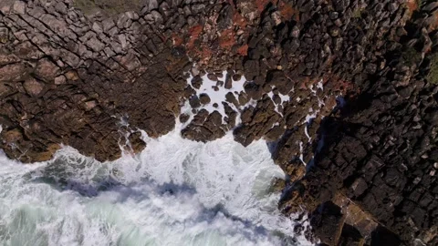 Aerial drone top down view of slow motion waves crashing against rocky shoreline Stock Footage 288455015