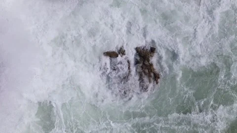 Aerial drone top down view of slow motion waves crashing against rocky shoreline Video stock 288455890
