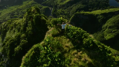 Aerial drone tracking shot of a man standing with outstretched arms on a grassy 库存影片 335708080