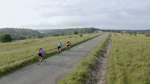 Aerial drone tracking shot of three cyclist cycling along a country road Stock Footage 128017767