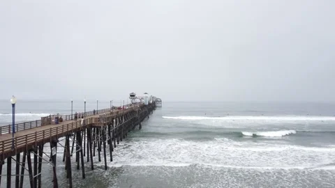 Aerial drone view alongside Oceanside Pier with surfing in foreground 스톡 동영상 157833731
