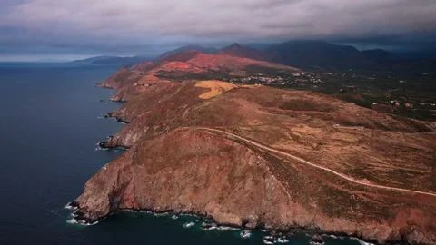 Aerial drone view of a bare headland and rugged coastline below mountains Stock Footage 339289646