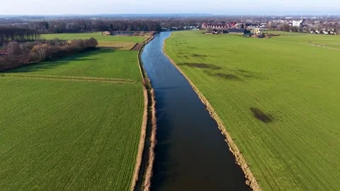 An aerial drone view capturing a long canal flowing through flat green pastures Stock Footage 336406938