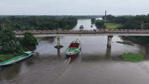 Aerial drone view of a cargo boat passing under a river bridge in village Stock Footage 341520871
