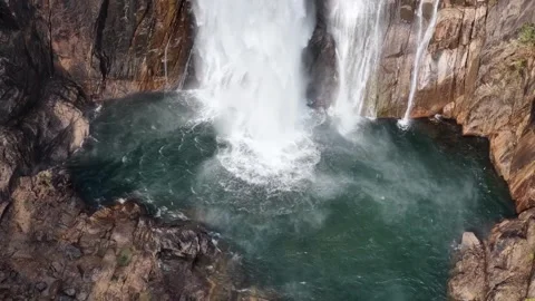 Aerial drone view of cascading waterfall plunging into vibrant green pool Stock Footage 336563277