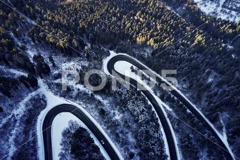Aerial drone view of a curved winding road through the forest high up in the Stock Photos
