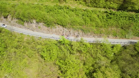Aerial drone view of cyclists riding along a winding mountain road through a Stock Footage 342264706