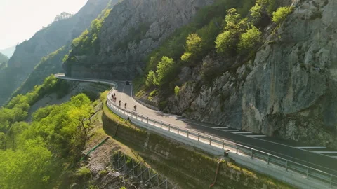 Aerial drone view of cyclists riding along a winding mountain at sunset Stock Footage 342266125