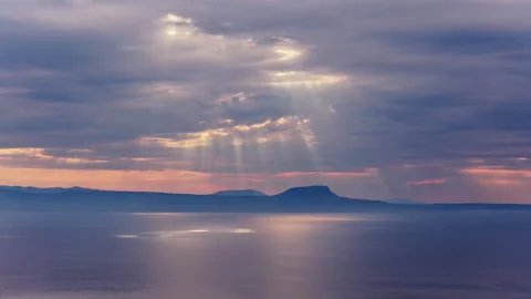 Aerial drone view of dramatic sun rays breaking through clouds over the calm Видео 339288415