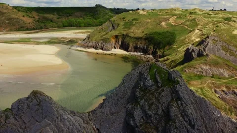 Aerial drone view flying over green cliffs onto a huge sandy beach at low tide Stock Footage 191665072