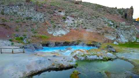 Aerial: Drone View Of Hot Spring Emitting Smoke Near Hill Against Sky At Sunset Stock Footage 249354783