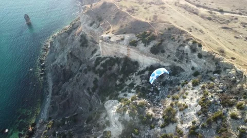Aerial drone view of a man flying a white and blue paraglider over a hill and Stock Footage 170876002