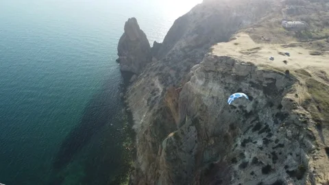 Aerial drone view of a man flying a white and blue paraglider over a hill and Stock Footage 170995079