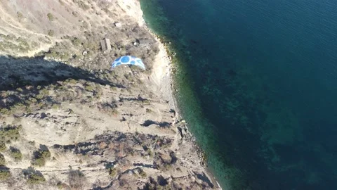 Aerial drone view of a man flying a white and blue paraglider over a hill and Stock Footage 171103631