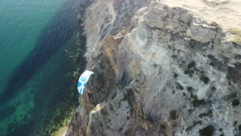 Aerial drone view of a man flying a white and blue paraglider over a hill and Stock Footage 171208005