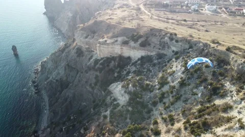 Aerial drone view of a man flying a white and blue paraglider over a hill and Stock Footage 171367523