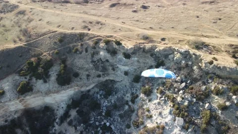 Aerial drone view of a man flying a white and blue paraglider over a hill and Stock Footage 171444701
