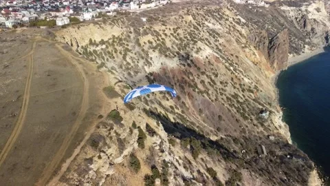 Aerial drone view of a man flying a white and blue paraglider over a hill and Stock Footage 171745261