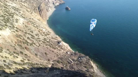 Aerial drone view of a man flying a white and blue paraglider over a hill and Stock Footage 171961906