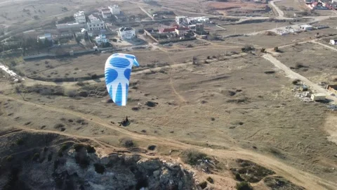 Aerial drone view of a man flying a white and blue paraglider over a hill and Stock Footage 172010482