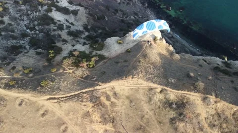 Aerial drone view of a man flying a white and blue paraglider over a hill and Stock Footage 172128902